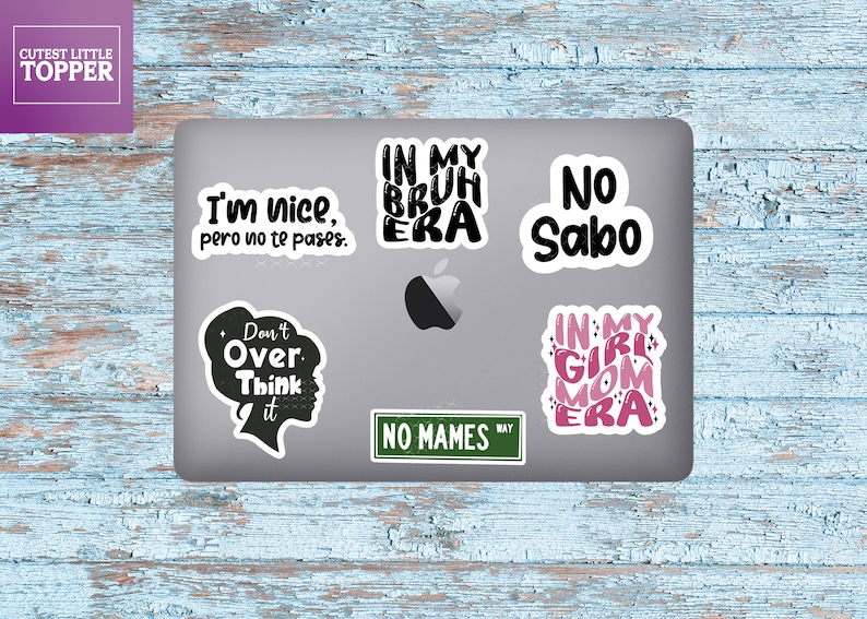 May include: A silver laptop with six stickers on it. The stickers are black and pink with various phrases, including "I'm nice, pero no te pases", "In my bruh era", "No Sabo", "Don't over think it", "No Mames", and "In my girl mom era".