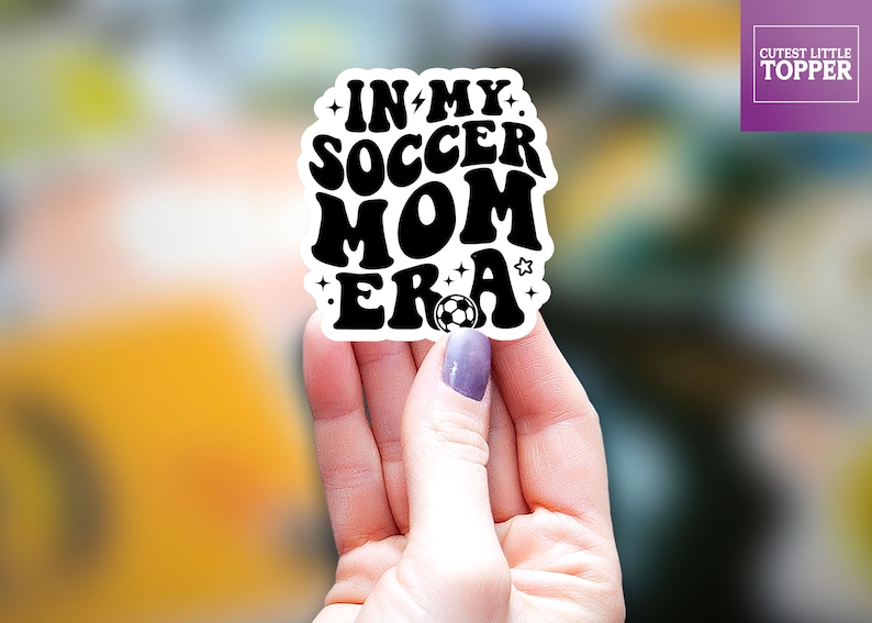 May include: Black and white sticker with the text "In My Soccer Mom Era" with a football graphic.