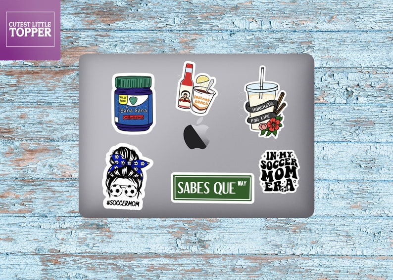 K&ouml;nnte beinhalten: Ein Laptop mit sechs Aufklebern. Die Aufkleber zeigen eine Frau mit einem Dutt und Fu&szlig;ball-Sonnenbrillen, ein Stra&szlig;enschild mit der Aufschrift "Sabes Que", eine Flasche Medizin, eine Tasse Horchata, eine Tasse Instantnudeln und einen Aufkleber mit der Aufschrift "In My Soccer Mom Era".