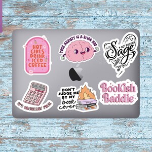 May include: A set of six pink and black laptop stickers with various designs and text. The stickers include a brain with the text "Your anxiety is a bring hoe", a calculator with the text "Girl Math, It's basically free", a stack of books with flames and the text "Don't judge me by my book covers", a heart with the text "Sage, Not enough for this", a cup of iced coffee with the text "Hot girls drink iced coffee", and a stack of books with the text "Bookish Baddie".