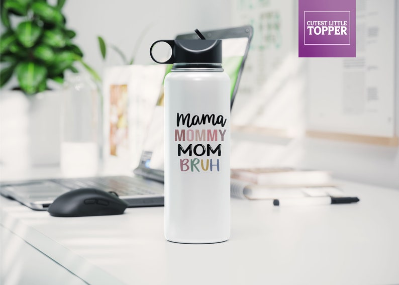 May include: White stainless steel water bottle with a black lid and a carrying handle. The bottle has the text "Mama Mommy Mom  Bruh" printed on it in colorful letters.