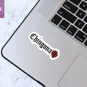 Pu&ograve; includere: Un adesivo bianco e nero con la parola "Chingona" in caratteri gotici, con una rosa rossa sotto. L'adesivo &egrave; su un laptop argentato.