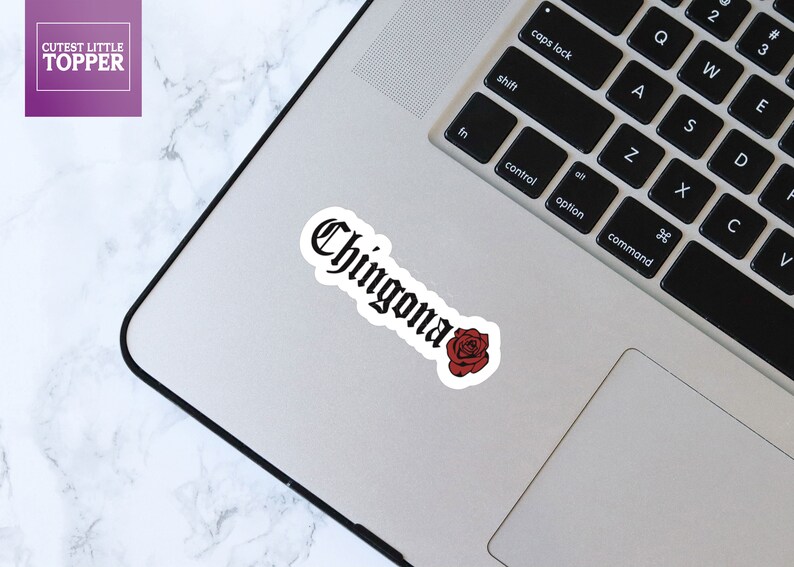 Pu&ograve; includere: Un adesivo bianco e nero con la parola "Chingona" in caratteri gotici, con una rosa rossa sotto. L'adesivo &egrave; su un laptop argentato.