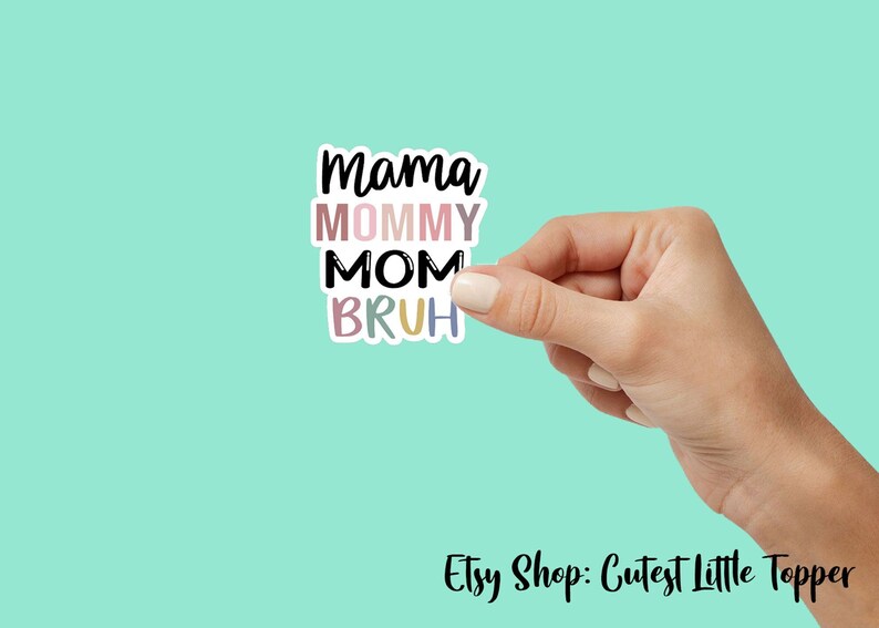 May include: A sticker with the text "Mama Mommy Mom Bruh" in black lettering with a colorful background. The sticker is being held by a hand.