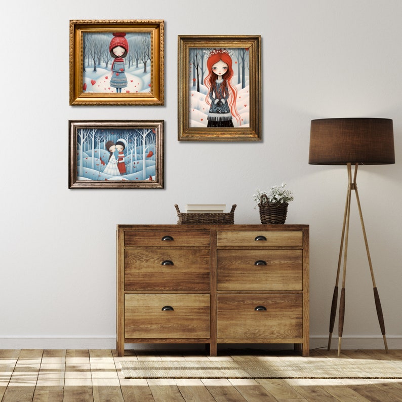 May include: Three framed illustrations of girls in winter scenes with red hearts. The illustrations are hanging on a white wall above a wooden dresser with three drawers.