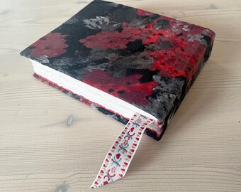 May include: A small, black and red floral patterned journal with a white ribbon bookmark. The ribbon has a repeating pattern of small hearts and a blue and white design.