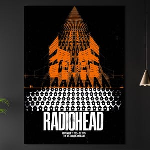 Op de afbeelding: Een ingelijste poster van Radiohead in oranje en zwart. Het ontwerp toont de bandnaam in het wit, met de datum en locatie van het concert eronder. Het kunstwerk hangt aan een donkere muur boven een bank.