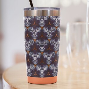 May include: A stainless steel tumbler with a navy blue, white, and orange geometric pattern. The tumbler has a coral-colored bottom and a black straw.