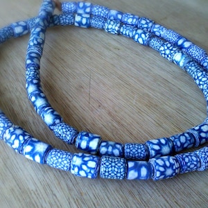 Peut inclure: Un collier composé de deux rangs de perles en céramique bleues et blanches. Les perles sont cylindriques et ont un fond blanc avec un motif bleu.