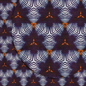 May include: A purple fabric with a white and orange geometric pattern. The pattern is made up of repeating stars with white stripes and orange accents.