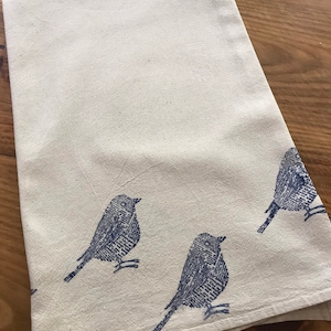 Puede incluir: Una toalla de cocina blanca con un dise&ntilde;o de p&aacute;jaro azul. Los p&aacute;jaros est&aacute;n impresos en un patr&oacute;n estilizado, casi pixelado.