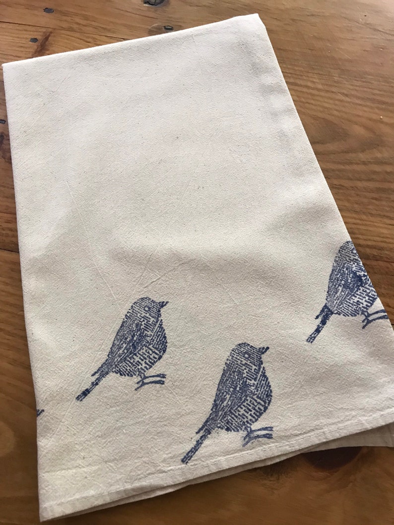 Puede incluir: Una toalla de cocina blanca con un dise&ntilde;o de p&aacute;jaro azul. Los p&aacute;jaros est&aacute;n impresos en un patr&oacute;n estilizado, casi pixelado.