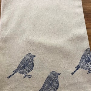 Puede incluir: Un pa&ntilde;o de cocina de algod&oacute;n blanco con tres siluetas de p&aacute;jaros azules impresas en &eacute;l.