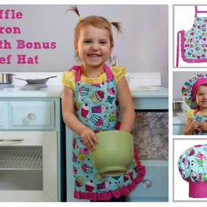 May include: A child wearing a turquoise and pink apron with a cupcake pattern and a matching chef hat. The apron has a ruffle trim. The child is holding a green bowl. The text "Ruffle Apron With Bonus Chef Hat" is in the top left corner of the image.