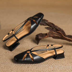 May include: A pair of black leather sandals with a square toe and a low, block heel. The sandals feature cut-out details on the vamp and a thin ankle strap. The interior is a light tan color.