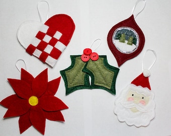 May include: Five felt Christmas ornaments: a red and white heart, a green holly leaf with red buttons, a red and white Santa face, a red ornament with a snowy scene, and a red poinsettia.
