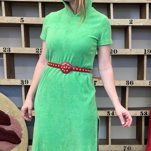 Puede incluir: Un vestido maxi de toalla verde con un cintur&oacute;n rojo tachonado. El vestido tiene cuello alto y mangas cortas. El vestido tiene una abertura lateral.