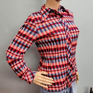 May include: A long-sleeved button-down shirt with a red, white, and blue plaid pattern. The shirt has a classic collar and is buttoned up the front. The fabric appears to be a lightweight material.