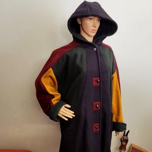 以下が含まれることがあります： パッチワークデザインのフード付きコート。バーガンディ、ダークグリーン、マスタードイエロー、ディープパープルのパネルが特徴です。コートはボタン留めで、マネキンに展示されています。フードは無地のダークパープルです。