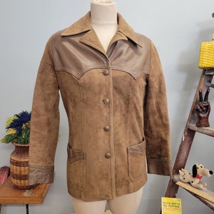 May include: A brown suede jacket with a brown leather collar and pockets. The jacket has a button-up front and long sleeves.