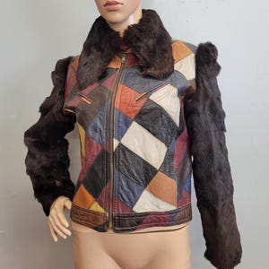 May include: A vintage patchwork leather jacket with a brown fur collar and sleeves. The jacket features a colourful geometric pattern of squares in various colours, including red, blue, and brown. It has a zip closure.