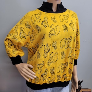 May include: Yellow sweater with black elephant and zebra pattern. The sweater has a black turtleneck and black cuffs. The sleeves are three-quarter length. The sweater is displayed on a mannequin.