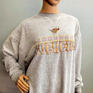 May include: A white ceramic mug with a black handle and the text "But First, Coffee" in a bold, black font. The mug is set against a blurred background, suggesting a cozy setting. The mug appears to be approximately 4 inches tall.