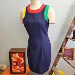 May include: A vintage navy blue dress with a color block design. The dress features a red neckline, yellow shoulder strap, and green shoulder strap. The dress is sleeveless and has a fitted silhouette.