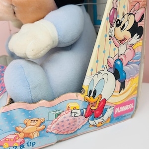 May include: A vintage Playskool toy box featuring Disney characters. The box has illustrations of Minnie Mouse, Donald Duck, and baby-themed items. A blue plush toy is visible inside the box. The box is designed for ages 2 & Up.