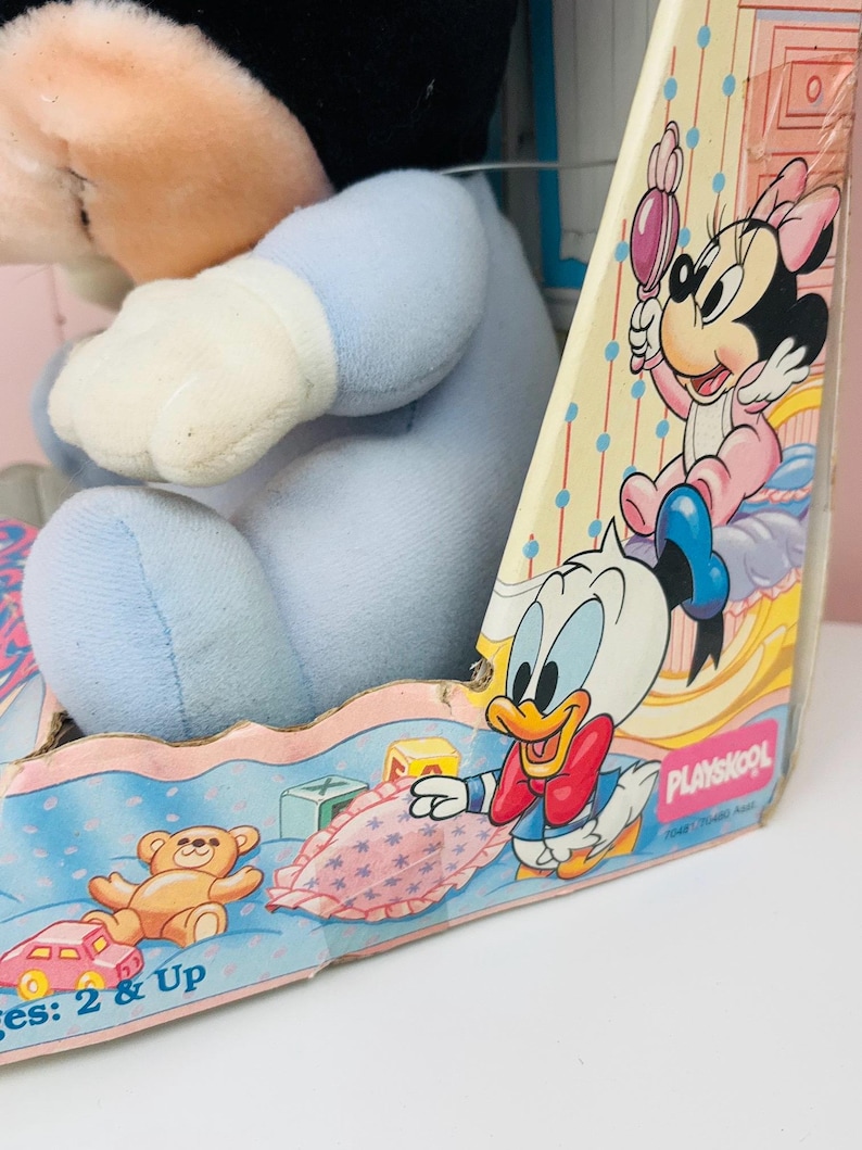 May include: A vintage Playskool toy box featuring Disney characters. The box has illustrations of Minnie Mouse, Donald Duck, and baby-themed items. A blue plush toy is visible inside the box. The box is designed for ages 2 & Up.