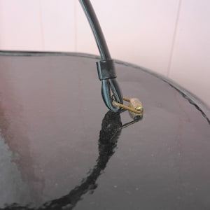 May include: Close-up of a black, glossy surface with a curved black handle and a small, gold-colored safety pin. The pin is attached to the handle. The surface reflects the handle and pin.
