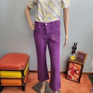 May include: A pair of vibrant purple flared pants with front pockets. The pants are displayed on a mannequin, showcasing their retro style. The fabric appears to be a soft, textured material. The pants are paired with a striped button-up shirt.