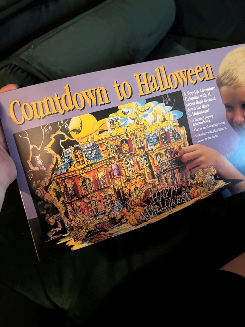以下が含まれることがあります： 「Countdown to Halloween」と題された、ハロウィーンをテーマにしたポップアップアドベントカレンダー。詳細な幽霊屋敷のイラスト、カボチャ、そして「Happy Halloween」の文字が特徴です。31個の秘密のフラップがあり、暗闇で光ります。