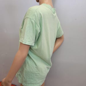 May include: A light green short-sleeved t-shirt. The shirt is made of a soft material and has a crew neck. The shirt is displayed on a mannequin against a gray background.