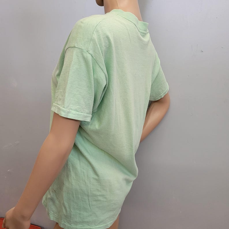 May include: A light green short-sleeved t-shirt. The shirt is made of a soft material and has a crew neck. The shirt is displayed on a mannequin against a gray background.