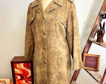 May include: A tan vintage coat with a button-up front, lapel collar, and shoulder epaulets. The coat has a mottled pattern and a tailored fit. The coat is displayed on a mannequin. A wooden box with an abstract design is in the background.