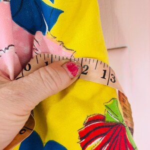 May include: A yellow fabric with a floral pattern featuring blue and red accents. A measuring tape shows a measurement of 5 cm. The fabric has a pink background with a blue bow.