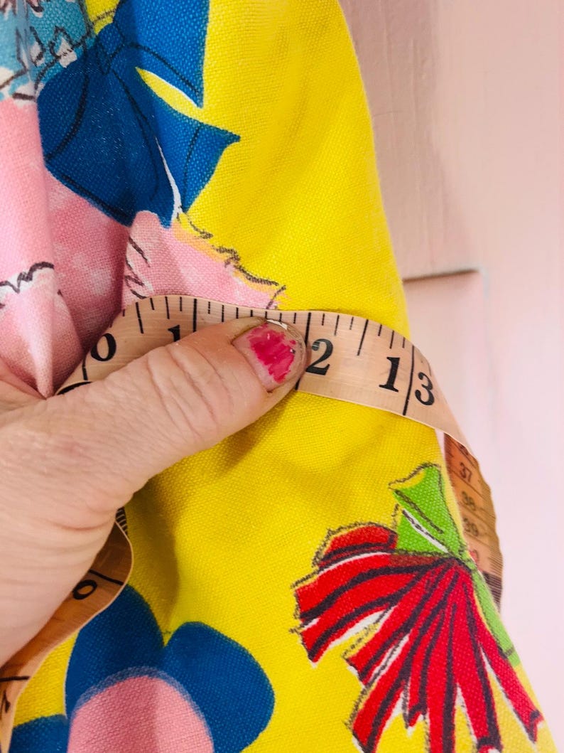 May include: A yellow fabric with a floral pattern featuring blue and red accents. A measuring tape shows a measurement of 5 cm. The fabric has a pink background with a blue bow.