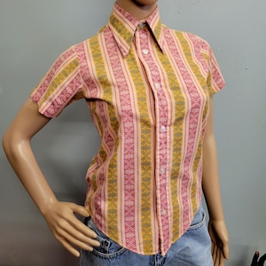 May include: A short-sleeved shirt with a vertical striped pattern in pink, yellow, and grey. The shirt features a pointed collar and white buttons. The fabric appears to be a woven material.