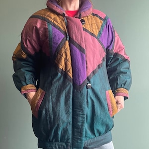 May include: A vintage, color-blocked jacket in shades of teal, purple, pink, and gold. The jacket features a quilted design on the shoulders and a large collar. It has two pockets and a button closure.