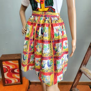 May include: A knee-length skirt featuring a vibrant grid pattern with alternating red and yellow squares. Each square contains detailed illustrations of roosters, floral arrangements, and vases in blue, green, and white. The skirt has a waistband.