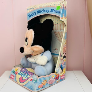 May include: A vintage Baby Mickey Mouse plush toy in its original box. The plush toy is wearing a blue outfit and a bib. The box features the words "Baby Mickey Mouse" and "Disney Babies". The box is decorated with cartoon characters.