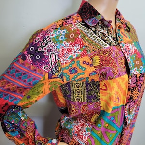 May include: A long-sleeved patchwork shirt in a vibrant array of colors, including orange, purple, pink, and teal. The shirt features a collared neckline and buttoned cuffs. The design incorporates paisley and floral patterns.