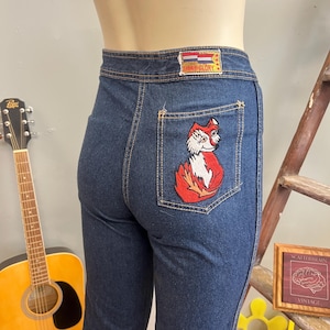 May include: Dark blue denim jeans with a fox patch on the back pocket. The jeans have a straight leg cut and a patch with the text "Faded Glory" on the back waistband. The fox patch is red, white, and black.