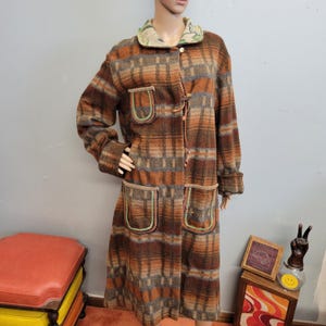 May include: A long, plaid coat in shades of brown, orange, and gray. The coat features two large pockets with green and tan trim, a floral-patterned collar, and toggle closures. The coat is displayed on a mannequin.