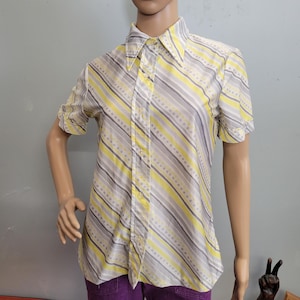 Può includere: Camicia a maniche corte con motivo a righe gialle, grigie e bianche. La camicia ha un colletto a punta ed è realizzata in un tessuto leggero. Le righe sono diagonali e si alternano tra linee piene e punteggiate.