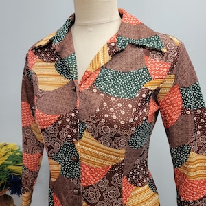 May include: A vintage button-down shirt with a patchwork design. The shirt features a variety of patterns in shades of brown, orange, green, and yellow. The long-sleeved shirt has a collared neckline and brown buttons.