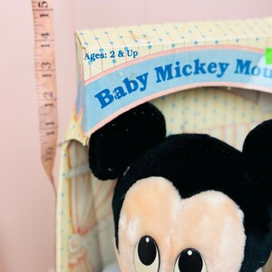 May include: A vintage Baby Mickey Mouse plush toy in its original box. The box is decorated with a pastel color scheme and the text "Baby Mickey Mouse". The plush toy has black ears and a cream-colored face.