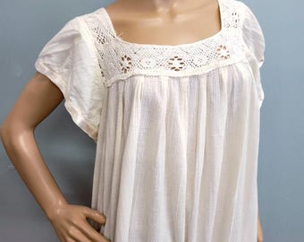 Puede incluir: Vestido color crema con cuello cuadrado y mangas cortas. El corpiño presenta un canesú de ganchillo con calados florales. El vestido tiene un corte holgado y fluido y está hecho de una tela ligera.