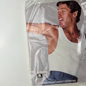 以下が含まれることがあります： 4枚の白い綿のタンクトップのパッケージ。パッケージには、白いタンクトップとブルージーンズを着た男性が写っています。パッケージのテキストは「4-Shirts」と「All Cotton/Royal Comfort/JCPenney」です。